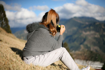 Woman sitting on mountain against sky