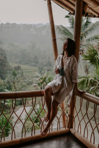 Full length of woman sitting on railing against mountain