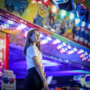 Low angle view of young woman looking away while standing in amusement park