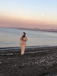 Man standing at beach against sky during sunset