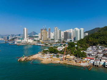 Buildings by sea against clear blue sky