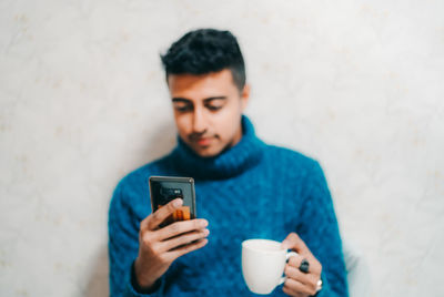 Young man using mobile phone against wall