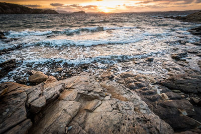 Scenic view of rocks at sea shore against sky during sunset