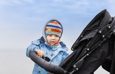 Low angle view of girl with baby stroller against sky