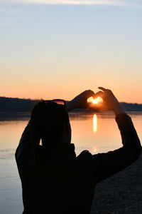 Rear view of woman standing by sea against sky during sunset