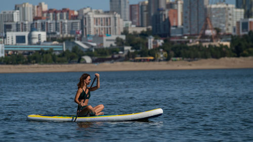 Man rowing boat in sea against city