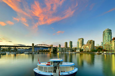 Boats in river by buildings against sky during sunset