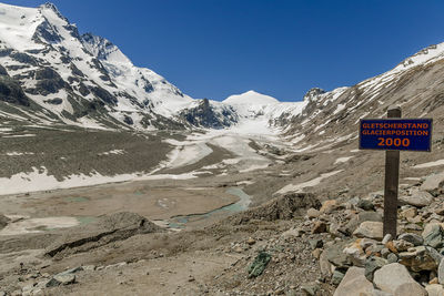 Road sign on snow covered mountain against clear sky