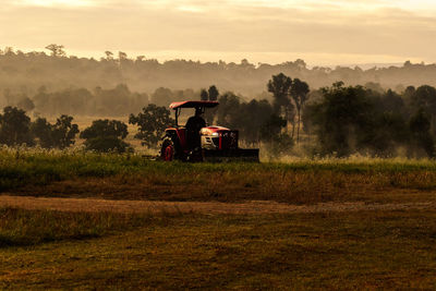 Tractor on field against sky during sunset