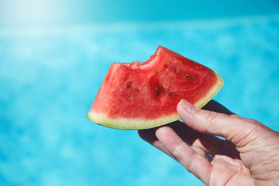 Cropped hand holding melon slice against swimming pool