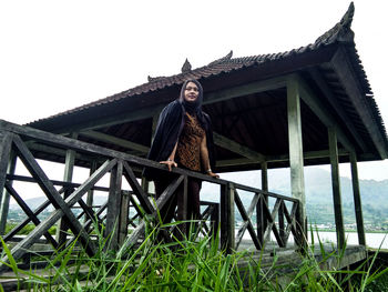 Woman leaning on railing by built structure against sky