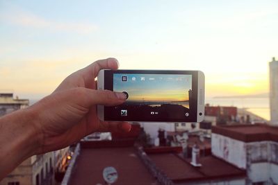 Close-up of hand holding smart phone against sky