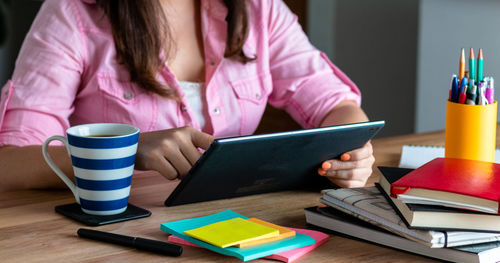 Midsection of woman using mobile phone while sitting on table