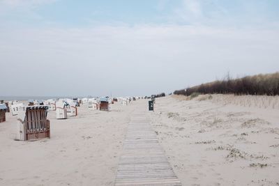 Hooded beach chairs on sand against sky