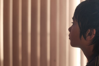 Thoughtful boy looking away while standing against curtain at home