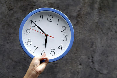Cropped hand of person holding clock against wall