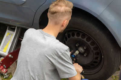 Rear view of man repairing car wheel