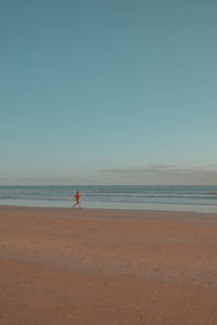 Rear view of woman standing at beach against clear sky