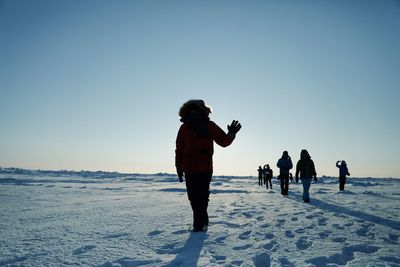 Silhouette hikers walking on snow covered landscape against clear blue sky during sunny day