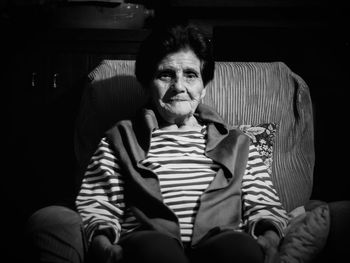 Portrait of senior woman relaxing on armchair in darkroom at home