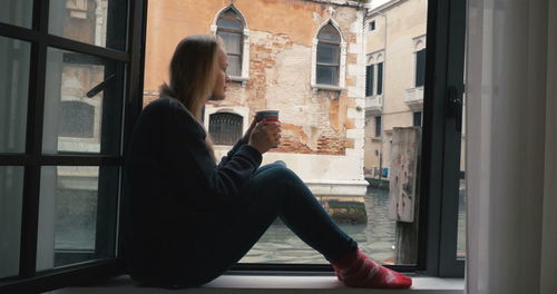 Side view of woman looking through window