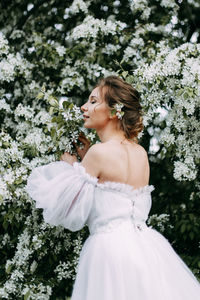 A beautiful young woman bride in a wedding dress walks alone in a blooming spring outdoor park