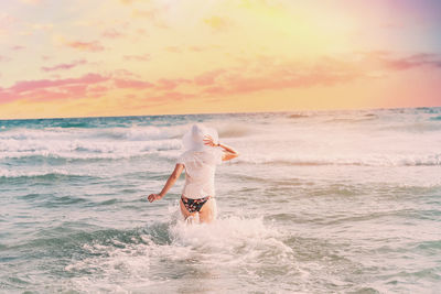 Rear view of man swimming in sea against sky during sunset