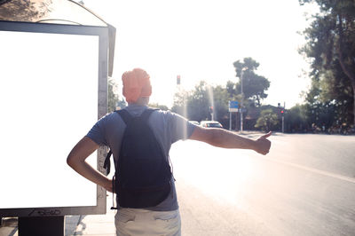 Rear view of man hailing at street on sunny day