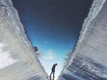 Upside down image of man standing in drying canal with reflection