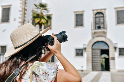 Rear view of young woman wearing summer clothes, using dslr camera to take photos on her travels