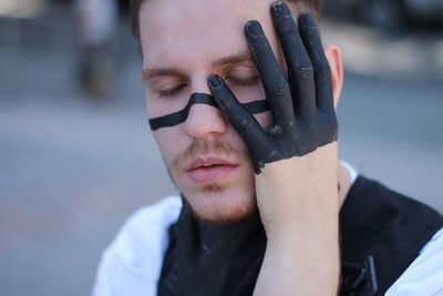 Close-up of man with eyes closed and face paint standing outdoors