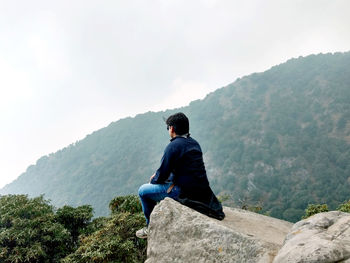 Rear view of man sitting on mountain against sky