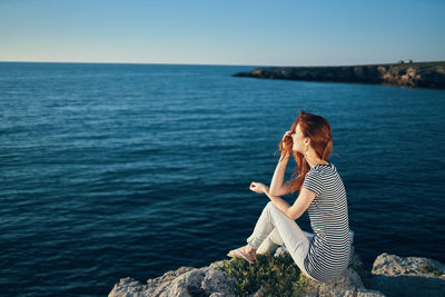 Full length of woman sitting on rock against sea