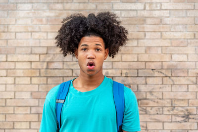 Afro latin male teenager doing a strange face against a wall