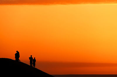 Silhouette people standing on sand dune at erg chebbi desert against sky during sunset