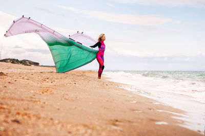 Rear view of woman standing at beach against sky