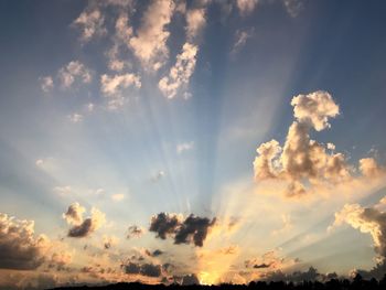 Low angle view of sunlight streaming through clouds during sunset
