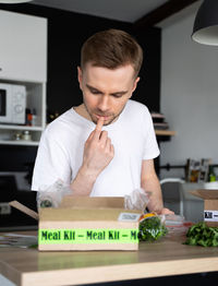 Thoughtful caucasian white man unpack online  food delivery.box with packed tuna,shrimp, vegetables