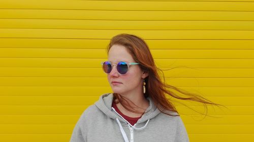 Close-up of young woman in sunglasses standing against yellow closed shutter