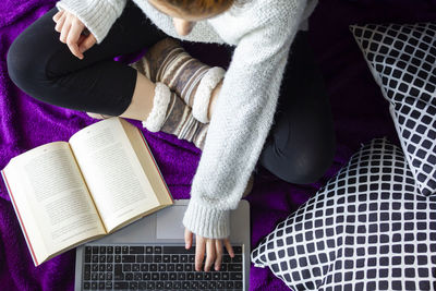 Top view of woman with comfort clothes sitting on bed with laptop and book