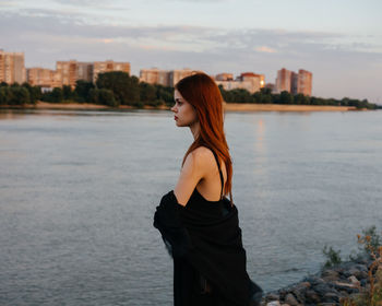 Side view of young woman standing in sea against city