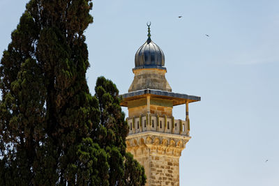 Low angle view of minaret and trees against clear sky