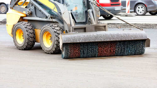 A compact grader at a construction site cleans the repaired section of the road from dirt .