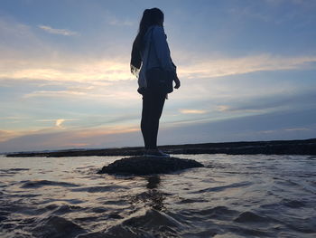 Rear view of woman standing in sea against sky