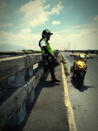 Man leaning by motor scooter on road against sky