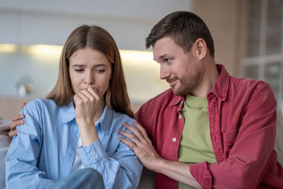 Crying, sad woman in depression while smiling husband lovingly hugs and calms her on sofa at home