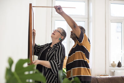 Heterosexual couple measuring painting while hanging on wall in living room