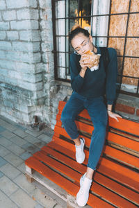 Young woman eating bun against brick wall