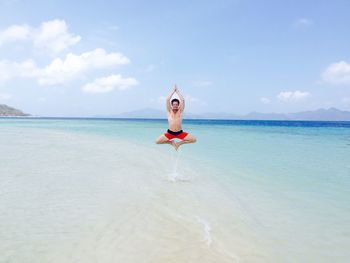 Shirtless man jumping on shore at beach against sky