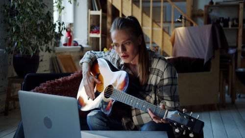 Woman learning guitar online at home